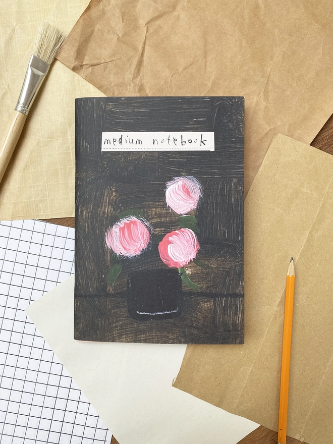 Notebook with dark cover and pink flowers on a desk with found paper around it.