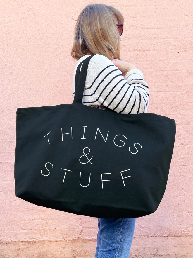 model holding an oversized black canvas tote bag with things and stuff slogan