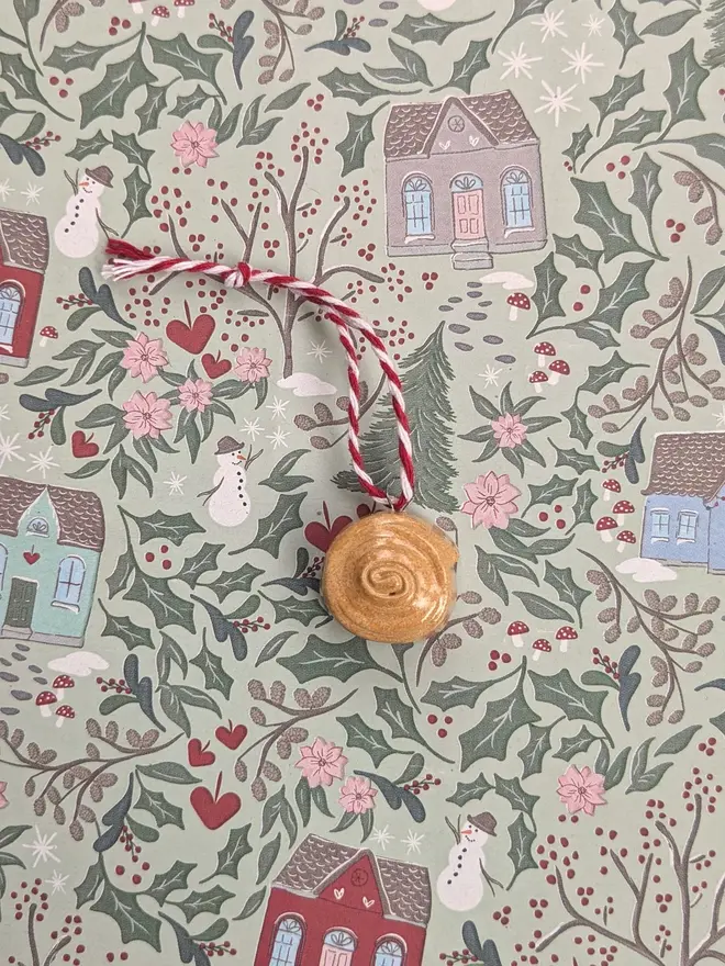 ceramic cinnamon bun christmas decoration. a close up image of a ceramic cinnamon bun hanging from red and white thread.