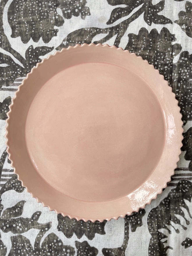 a rose gold scalloped edge dinner plate on a black and natural pattern cloth