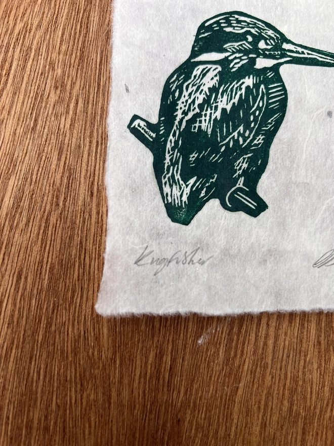 Close-up of a hand-printed green kingfisher lino print showing the carved detail, ink texture and natural grain of the handmade paper.