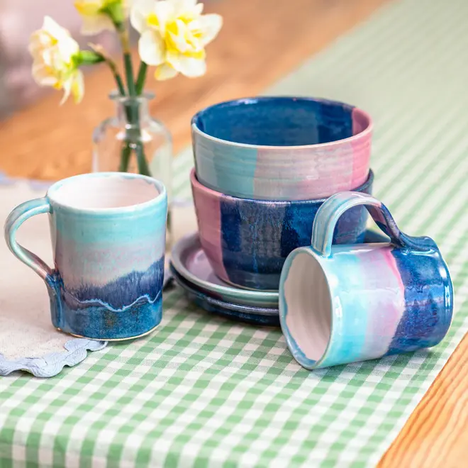 Landscape Breakfast (Set Of 2), a collection of colourful breakfast ceramics placed on a table. They are accompanied by a green table cloth and some flowers. 