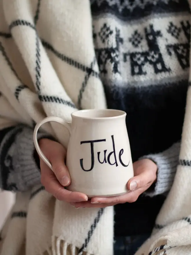 large personalised hand-thrown ceramic mug. mug painted with the name 'jude' and held in hands for scale.