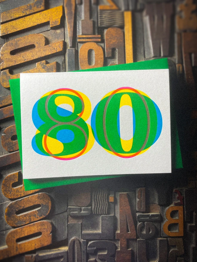 Handmade letterpress 80th birthday card featuring bold overlapping numerals printed in vibrant fluorescent cyan, magenta and yellow inks. Each card is individually hand printed using traditional letterpress techniques on luxury paper stock, creating a beautifully tactile finish with a subtle deboss and rich layered colours inspired by the CMYK printing process.