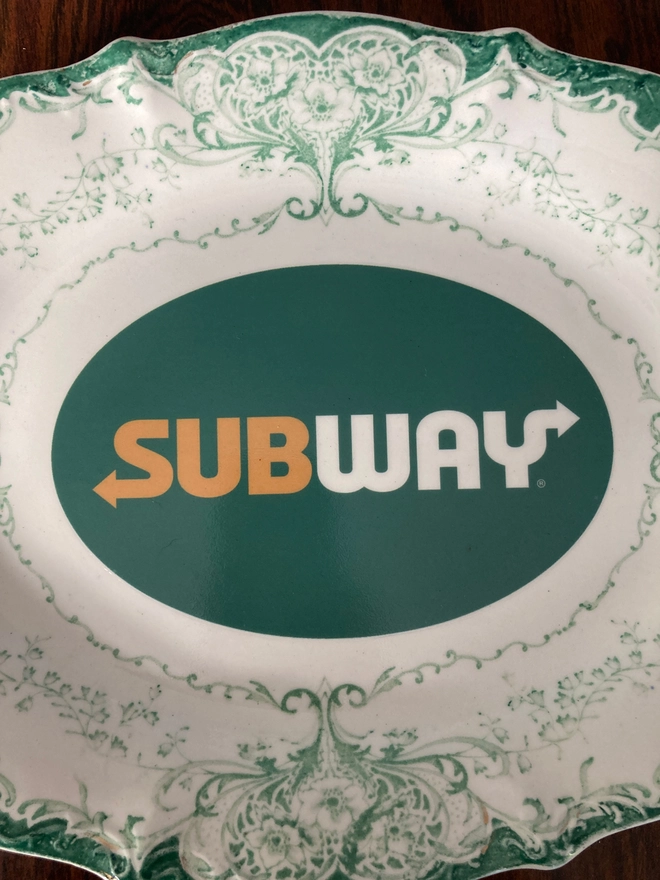 Close up of vintage decorative white and green china plate featuring a Subway logo