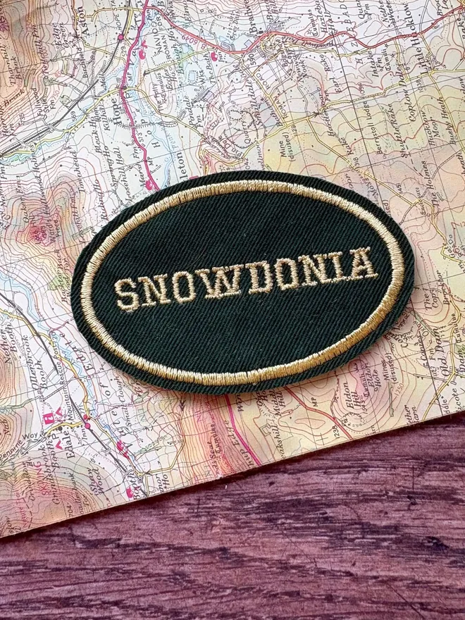 Green and cream custom location patch, with the wording Snowdonia, laying on a vintage map