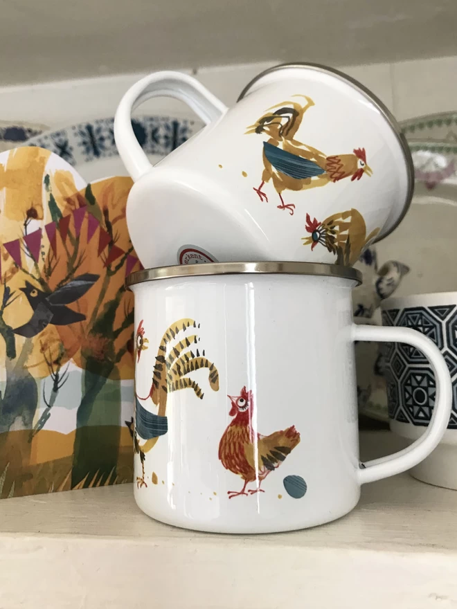 Stacked enamel mugs showing painterly cockerels design in mustard and blue and red