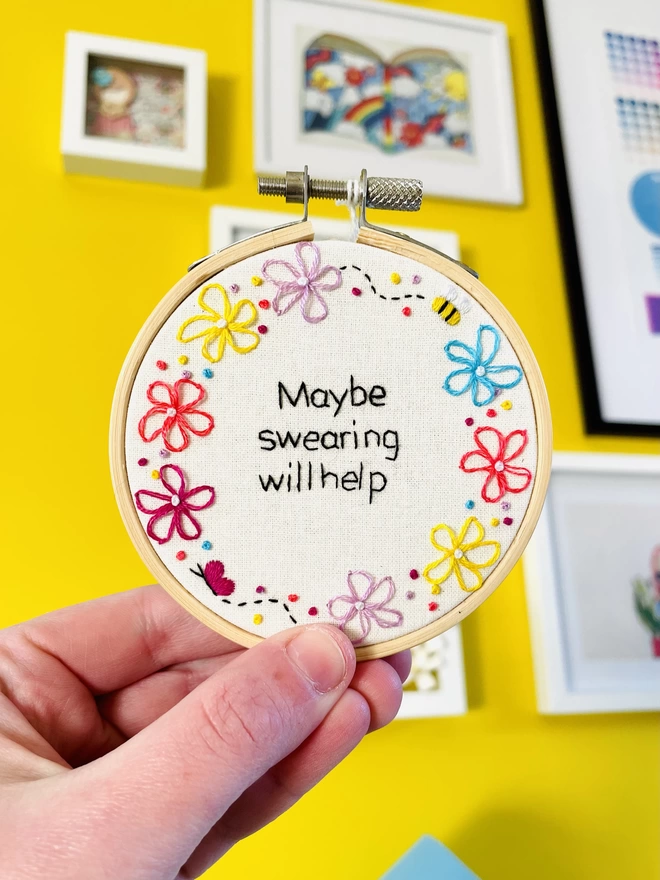 Hand embroidery hoop reads Maybe Swearing Will Help surrounded by colourful flowers and little bee and butterfly
