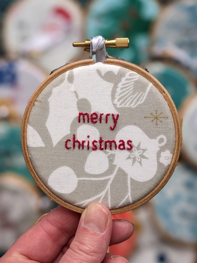 A hand embroidered hoop on Christmas fabric reading merry christmas