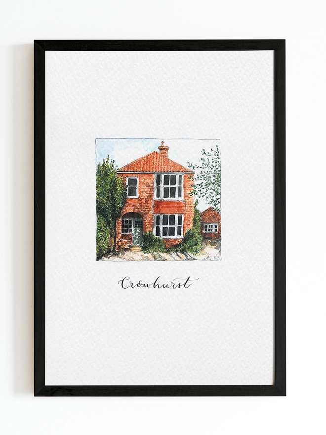 Black frame with white page inside and a red brick house in the centre painted in intricate watercolour details. Below black calligraphy lettering reads Crowhurst. The house is a red brick with teracotta roof and there is a small brick porch to a stepped back entrance door throgh and arch. 