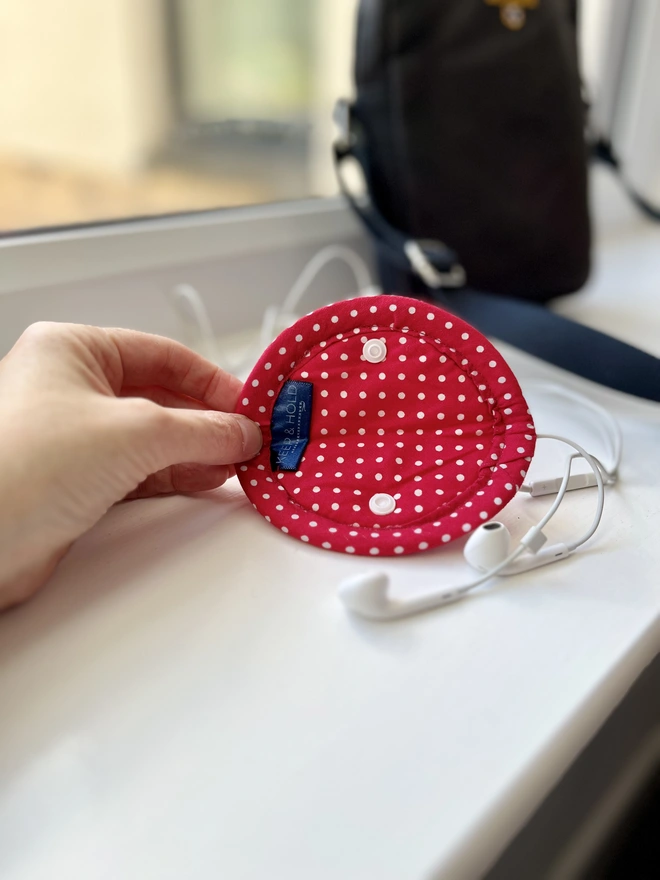 An open, circular, soft cotton fold-over earphone case showing red polka dot lining.