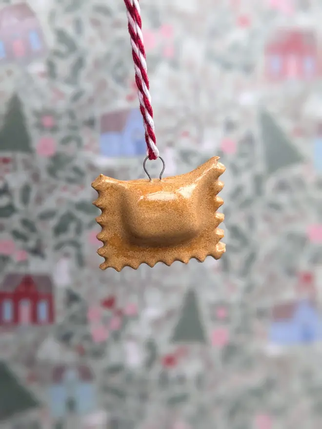 ceramic ravioli christmas decoration. a small pasta ornament hanging from red and white thread.