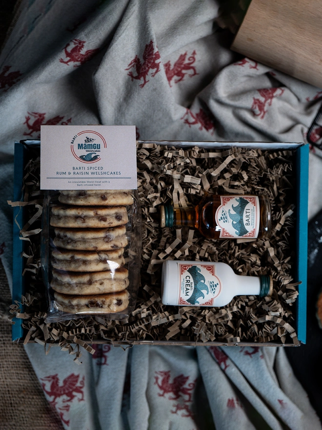 Barti Rum and Raisin Welsh Cakes and a miniature Bart Rum and Barti Cream in a teal gift box on a welsh dragon and beige table cloth 