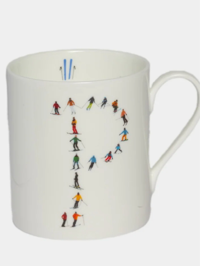 A simple white mug illustrated with a ‘P’ made of small, multicoloured skiers. The mug is set against a plain, white background.