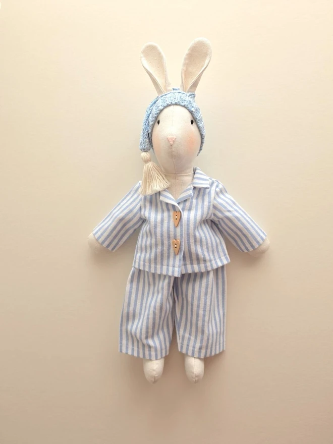 Full-length handmade linen Gerald Bunny wearing blue striped pyjamas and a pale blue knitted sleepy hat, handcrafted by Verity Isabelle.