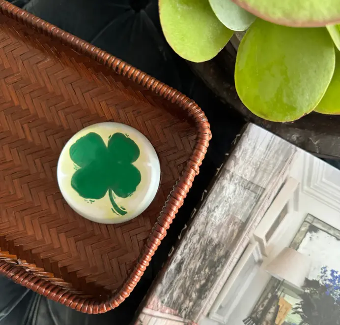 Round clover paperweights on a wooden trey beside a plant.