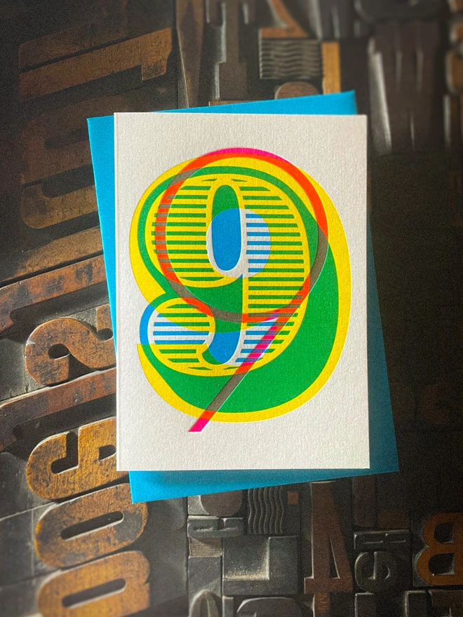 Handmade letterpress 9th birthday card featuring bold overlapping numerals printed in vibrant fluorescent cyan, magenta and yellow inks. Each card is individually hand printed using traditional letterpress techniques on luxury paper stock, creating a beautifully tactile finish with a deep impression and rich layered colours inspired by the CMYK printing process. Printed on a traditional letterpress from 1915. A wonderful artisan printed birthday card.