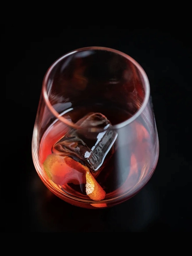 Damson Negroni, glass of negroni on a black surface. 