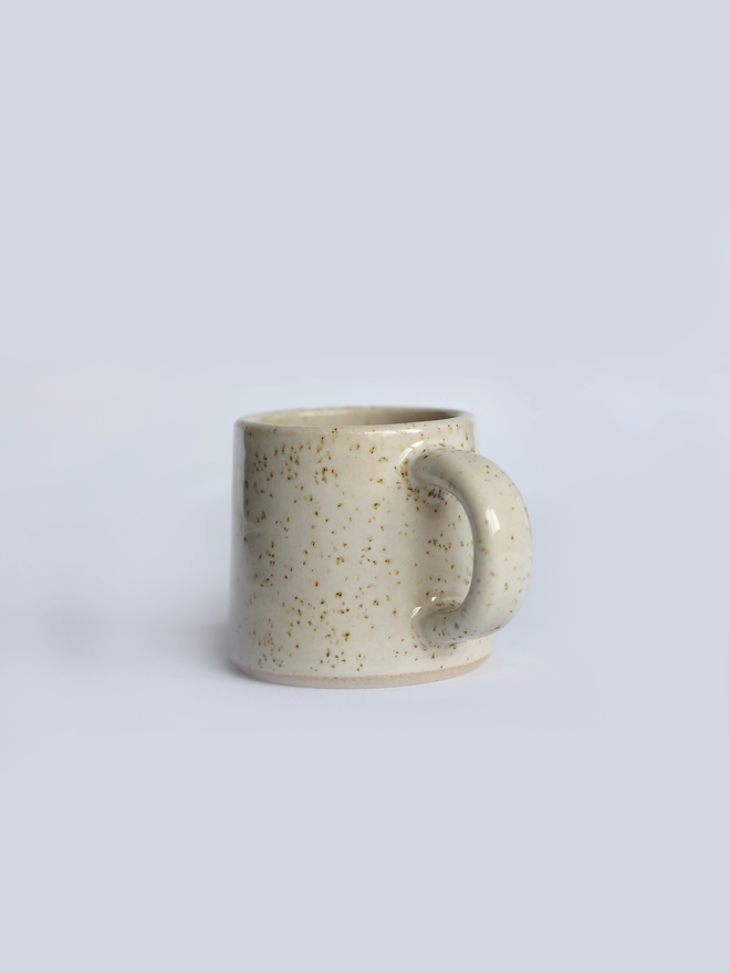 A handmade ceramic espresso mug in speckled pepper white glaze, with a chunky loop handle, photographed against a plain light grey background