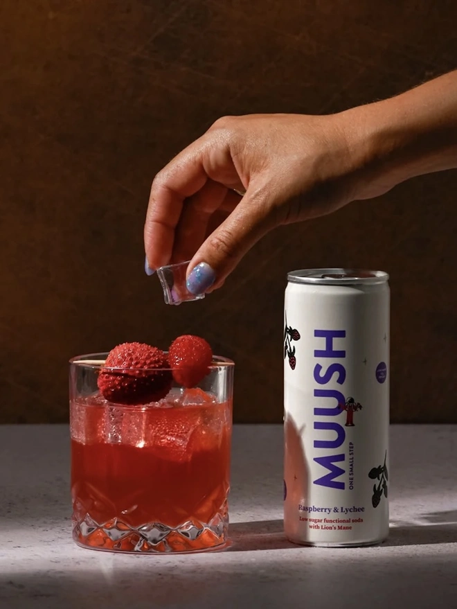 Raspberry & Lychee Cans (Pack Of 12), a raspberry and lychee soda sitting in a glass on a stone surface. 