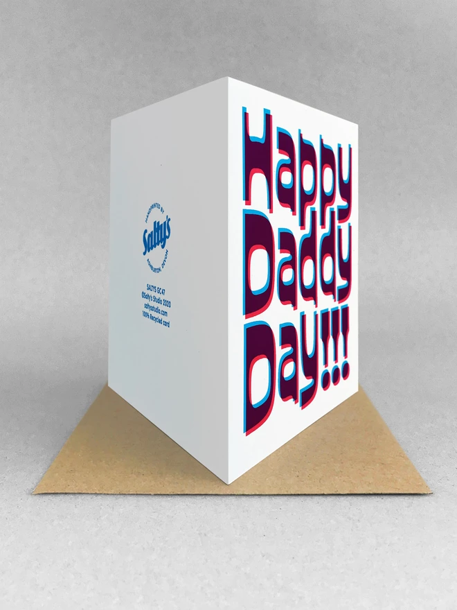 Rear view of a Happy Daddy Day screen printed cards. printed in magenta and cyan blue ink, a slight overlapped design to create this retro jolly card. Stood on a kraft brown envelope in a white studio background.