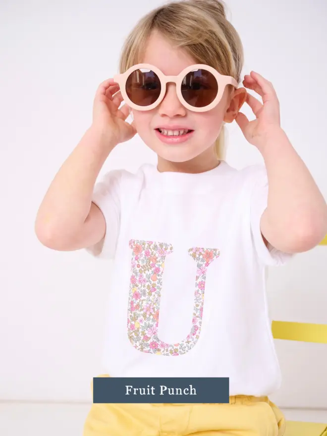 a 3 year old girl wearing a personalised kids white t-shirt with an initial cut from liberty floral print on the front