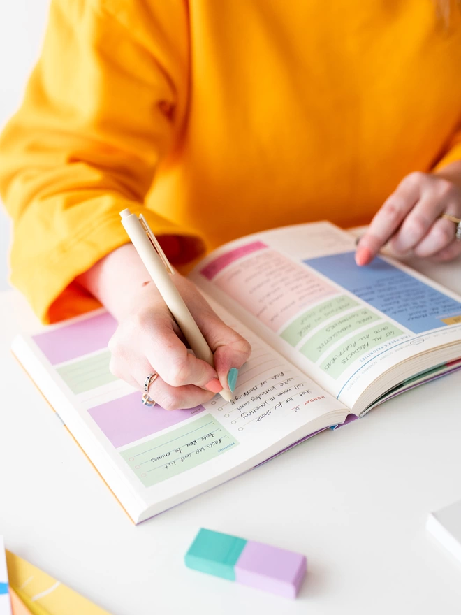 Writing inside colourful daily planner, planner has colourful spaces to plan your week, set priorities and track habits. 