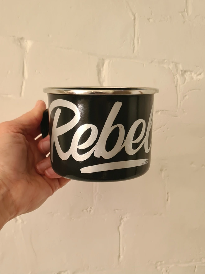 'Rebel' Enamel Mug, a colourful mug sitting on a white surface. held 