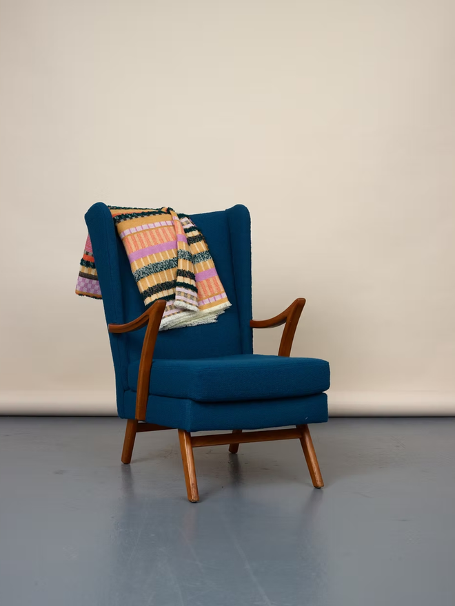 aednat lambswool blanket. a multi coloured patterned blanket, thrown over a blue chair.