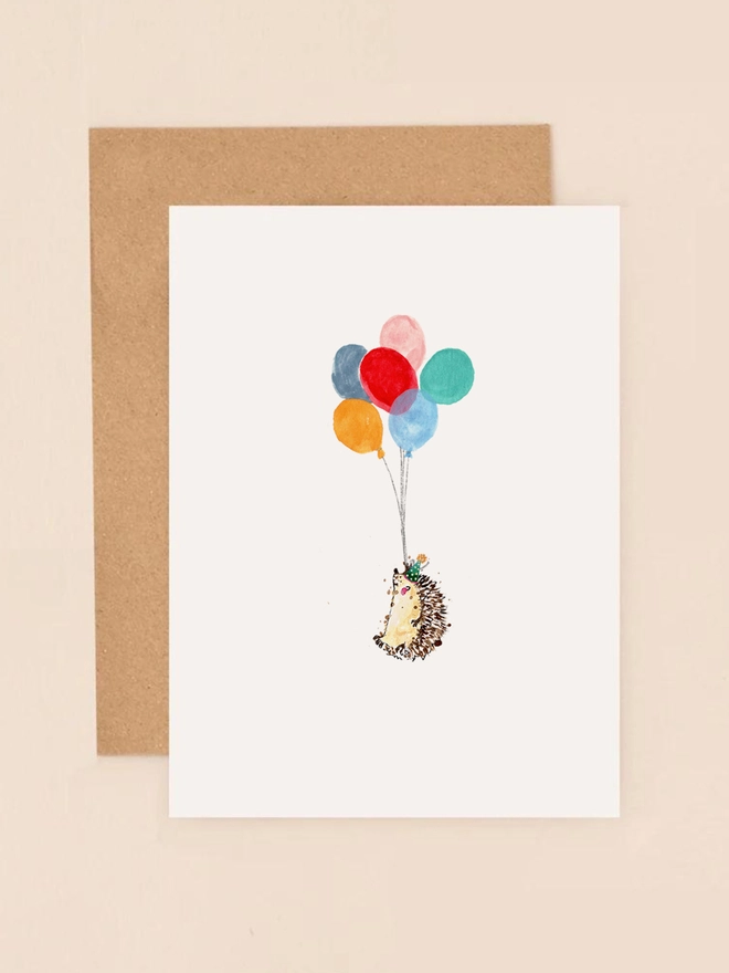 A delightful illustration of a hedgehog holding a bundle of colorful balloons, exuding a sense of joy and celebration. The hedgehog's cheerful expression and the vibrant hues of the balloons create a whimsical and festive atmosphere. The design is complemented by a soft, neutral background, enhancing the playful and heartwarming sentiment of the card.
