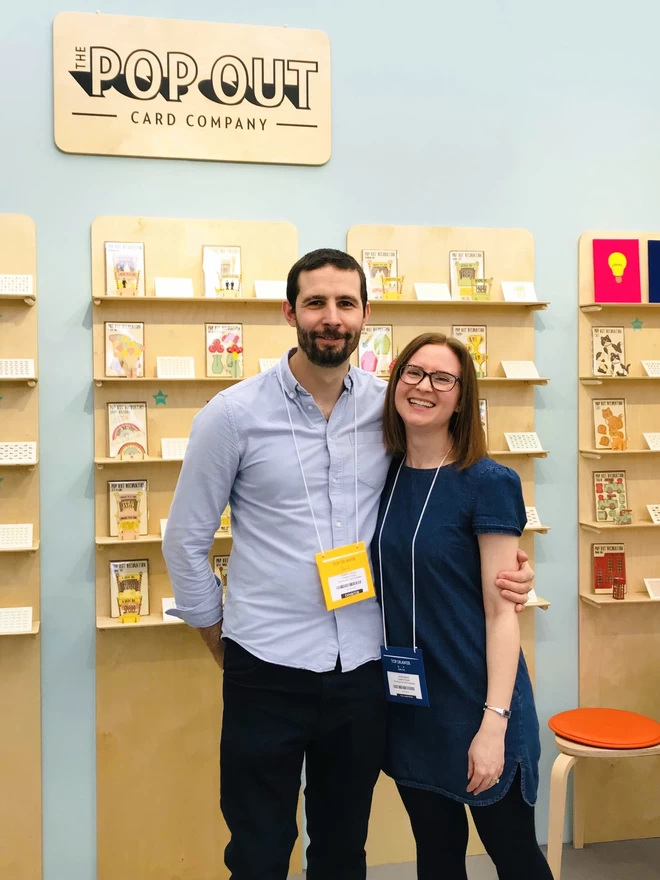 A man and a woman hugging whilst at a trade show event selling pop out greeting cards