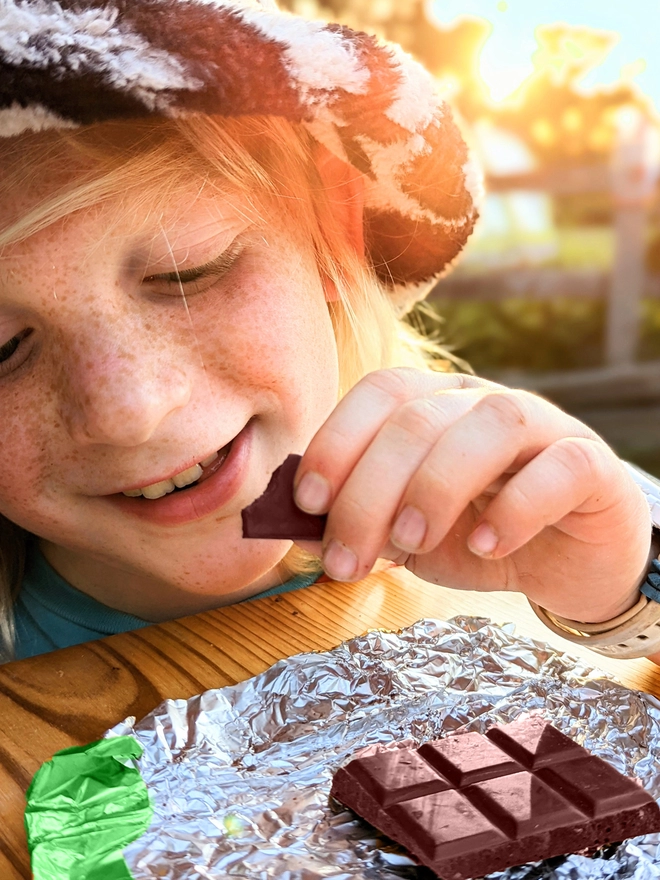 Happy young child opening green foil wrapped charity ruby chocolate bar