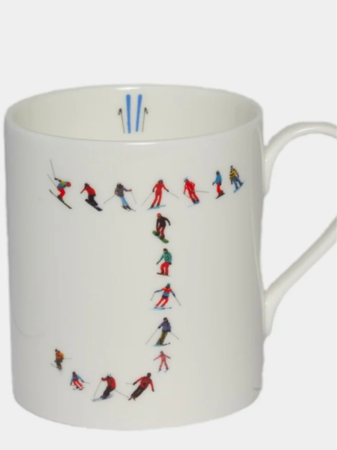 A simple white mug illustrated with a ‘J’ made of small, multicoloured skiers. The mug is set against a plain, white background.