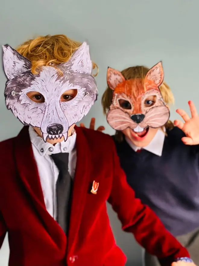 Cut And Create Forest Animals Children’s Masks, two young children posing playfully while wearing homemade paper animal masks of a grey wolf and an orange squirrel.