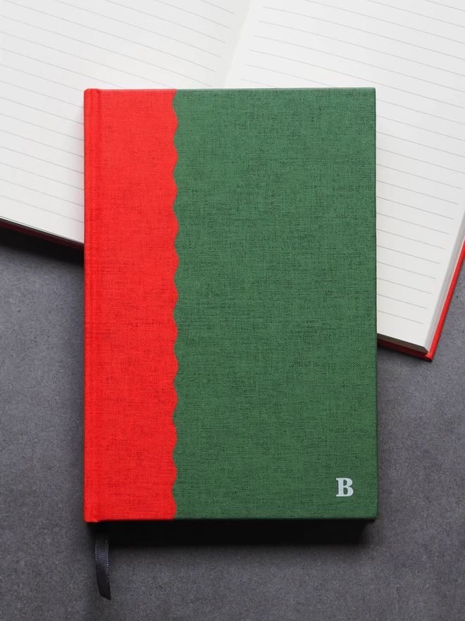 a hardcover two tone book, in green and red, with a scallop design, and the initial B stamped on the front in white ink
