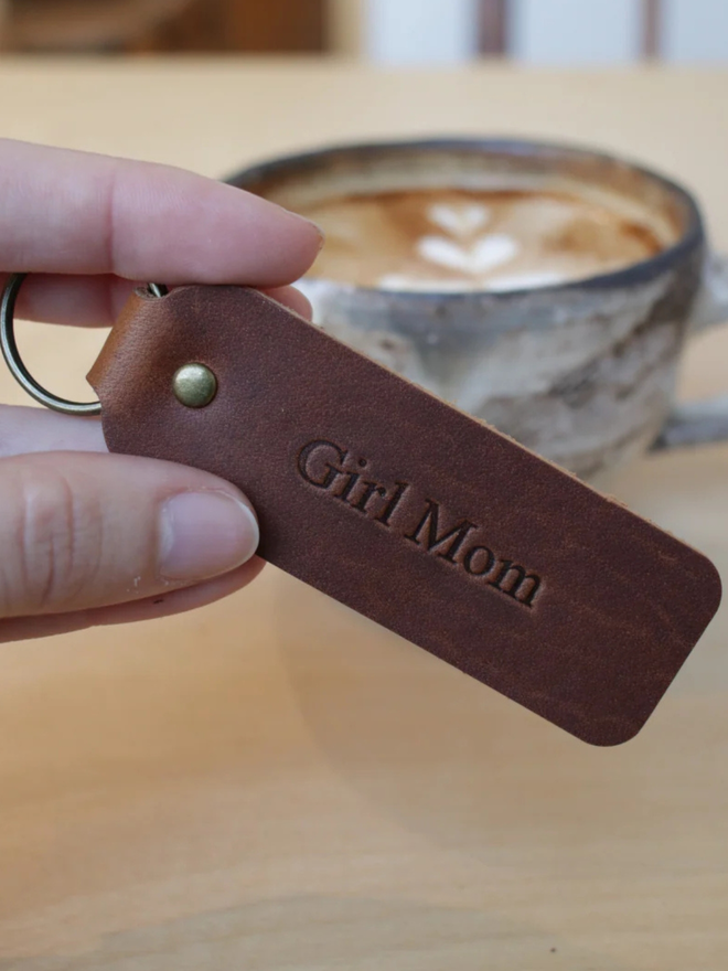 mother's day leather keyring. a hand holding a brown keyring embossed with 'girl mom'.