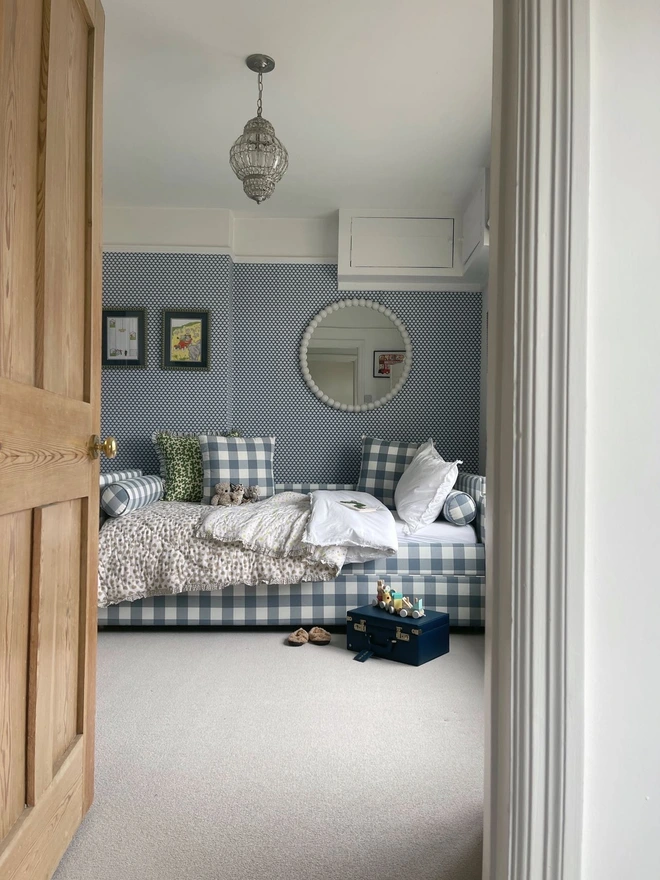 'The Posie' blue gingham upholstered children's bed. a blue gingham sofa-style bed for children featuring a duvet and cushions in a bedroom.