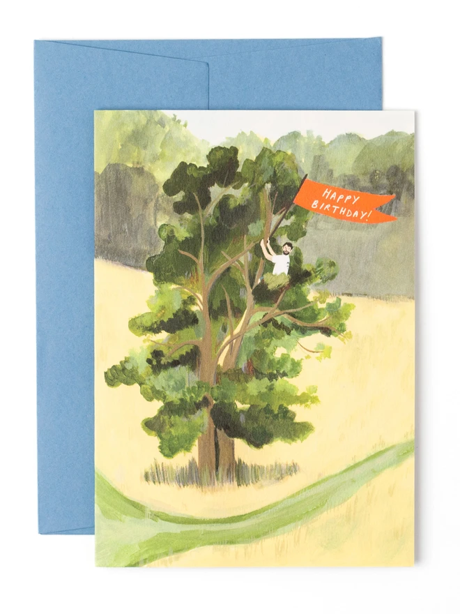 An illustrated birthday card. A tall tree stands in a field of dried grass. A man in a white t shirt has climed to the top of the tree and is waving a flag that reads "happy birthday"