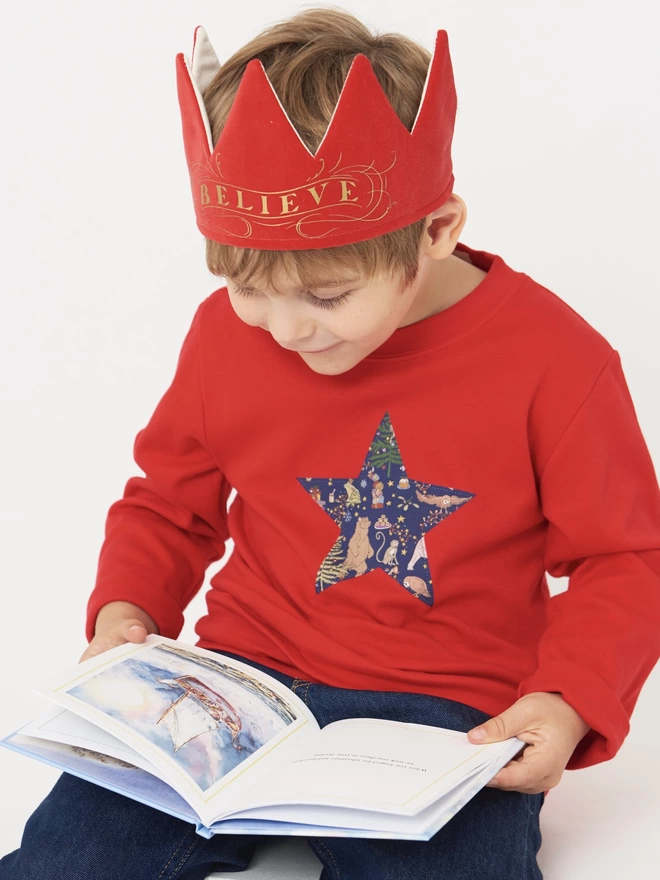 A little boy reading a christmas book wearing a red liberty Christmas print star tee