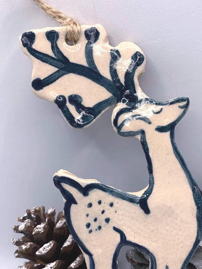 Handmade Ceramic Reindeer Ornament Scandinavian Folk Decor, a colourful reindeer decoration sitting on a plain surface joined by some acorns. 