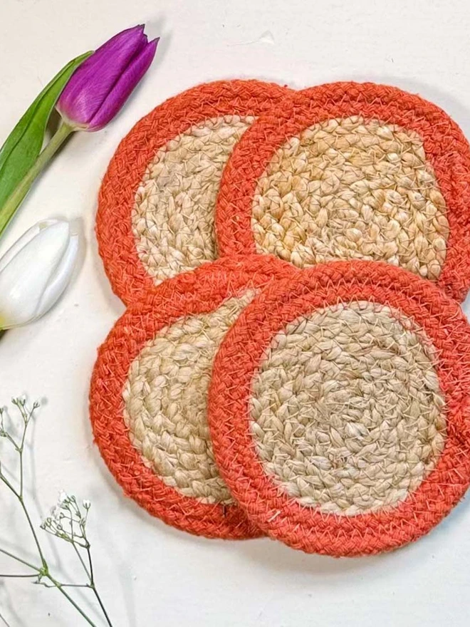 Seagrass coaster with orange rings, shown on a light surface with a tulip. 