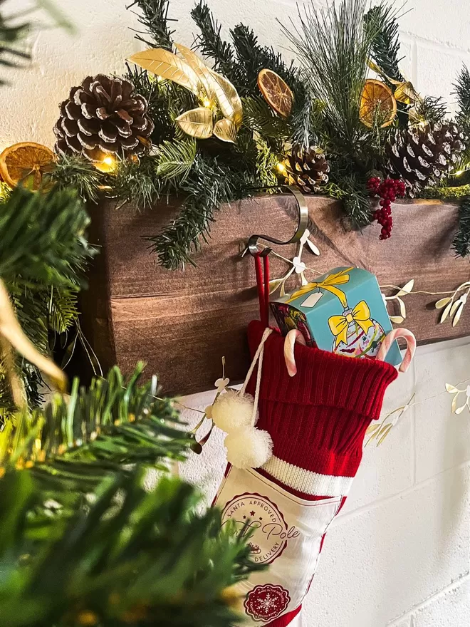 christmas stockings stuffed with candy canes & a Chocolate Christmas Babuble Box hanging on a wall next to a christmas tree with Chirstmas Decorations