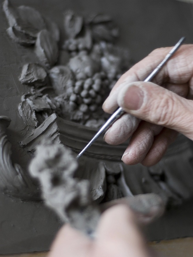 Sculptor modelling Still Life relief plaque in clay with fingers and modelling tools