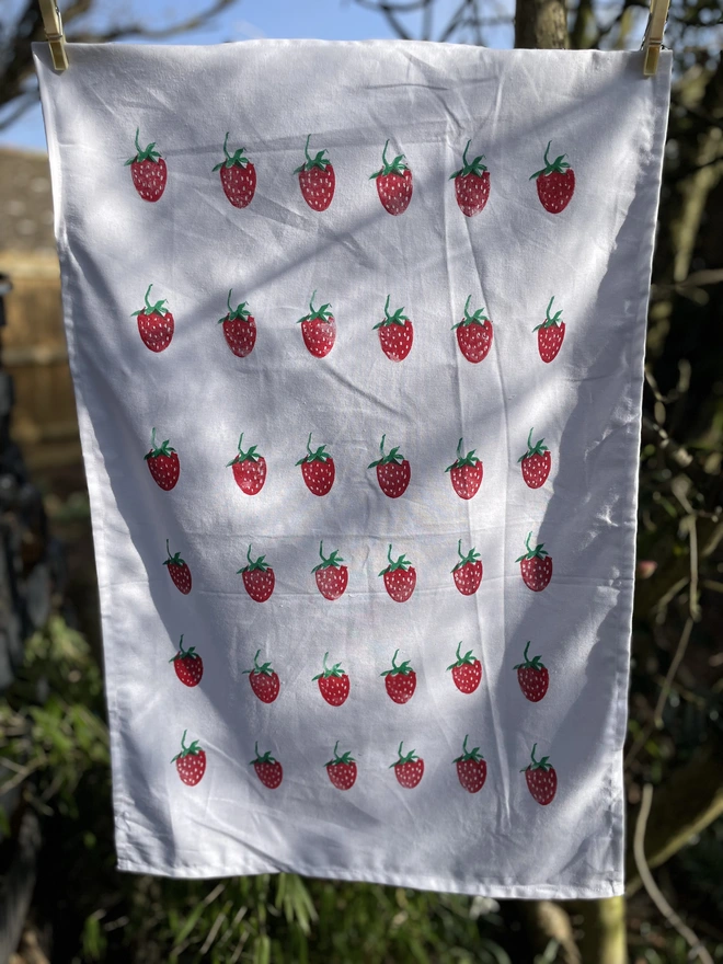 Kitchen tea towel with a strawberry pattern displayed outdoors in natural light.