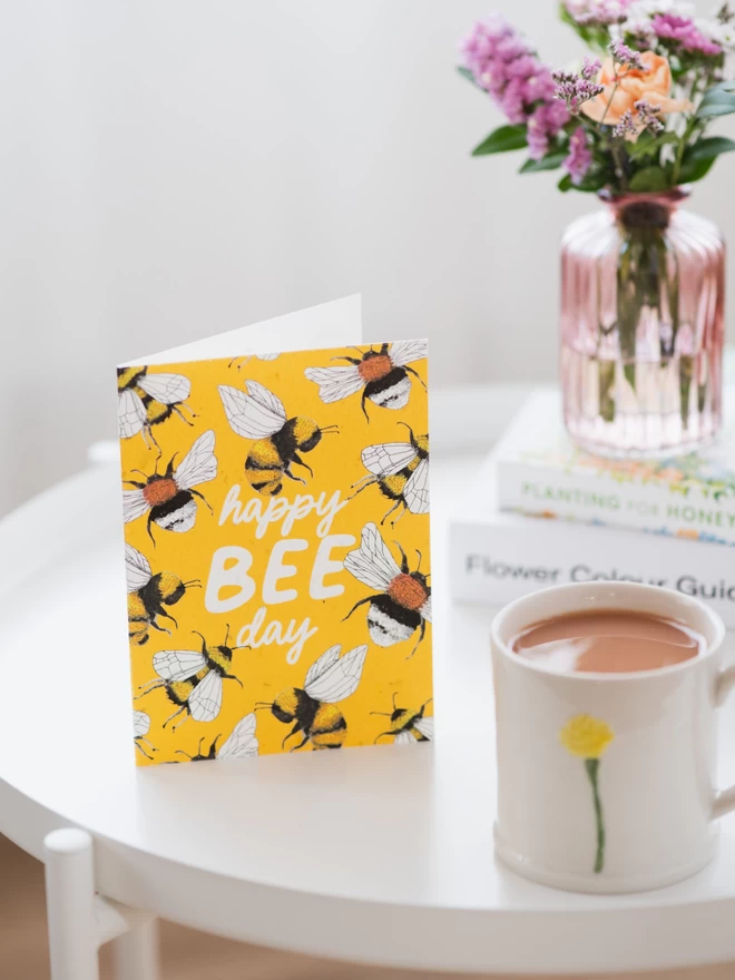 happy bee day plantable birthday card on white coffee table beside mug of tea