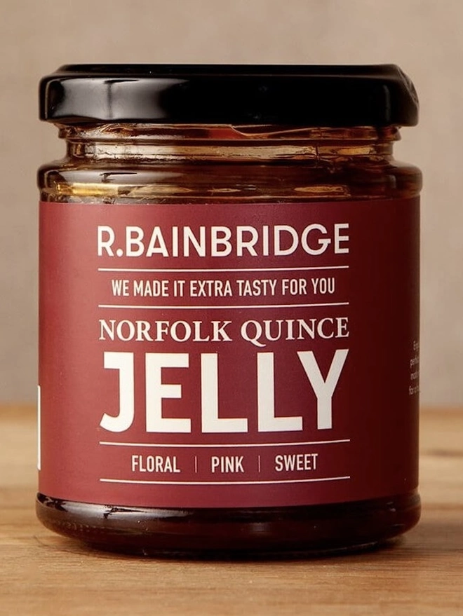 Norfolk Quince Jelly (Set Of 1, 2 Or 3), a jar of jelly sitting on a wooden surface against a plain backdrop. 