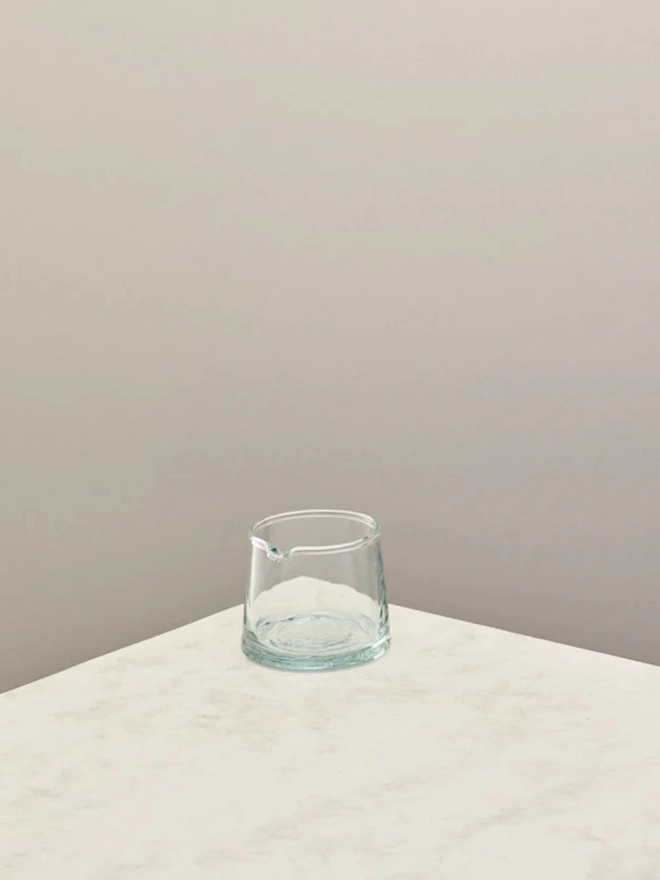 Glass Jugs (Set Of 2), a small clear glass jar sitting on a plain counter top against a grey backdrop. 