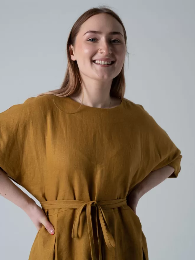 Midi length linen dress in golden colour. Self tie belt, pleated skirt and elbow length sleeves. Studio view sleeve batwing sleeve.