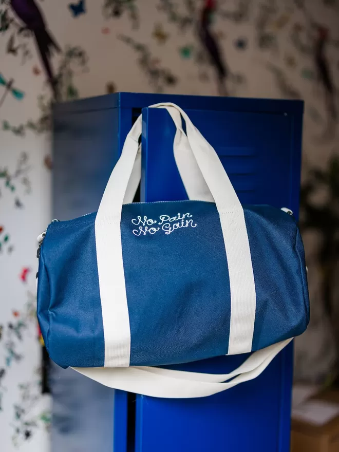 Navy Blue Duffel Bag with embroidered 'No Pain No Gain' hanging on a blue locker