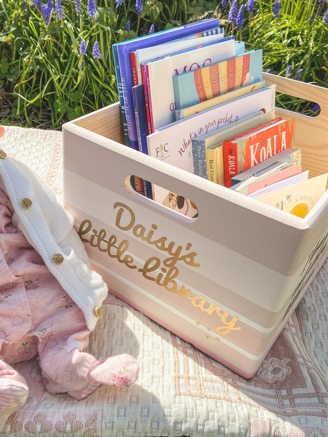personalised children's book storage box. a book storage box with personalised colours and text on a picnic blanket.
